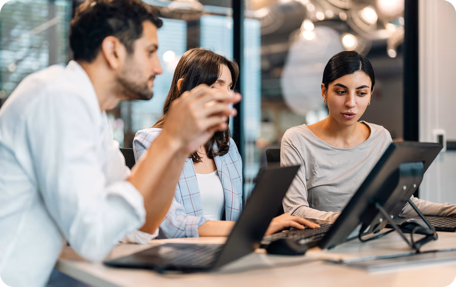 Three coworkers collaborating on laptops and a tablet in a modern office.