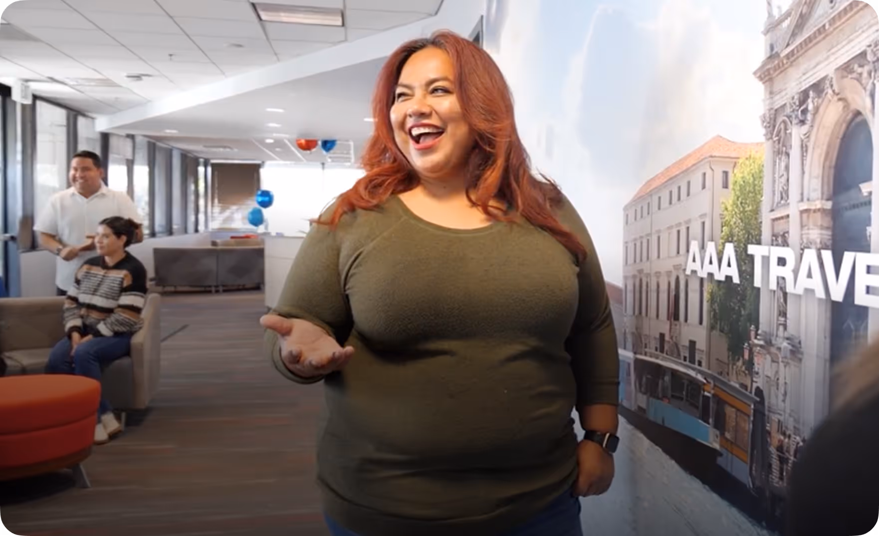 Smiling woman with red hair and green shirt standing in an office with a AAA Travel mural in the background.