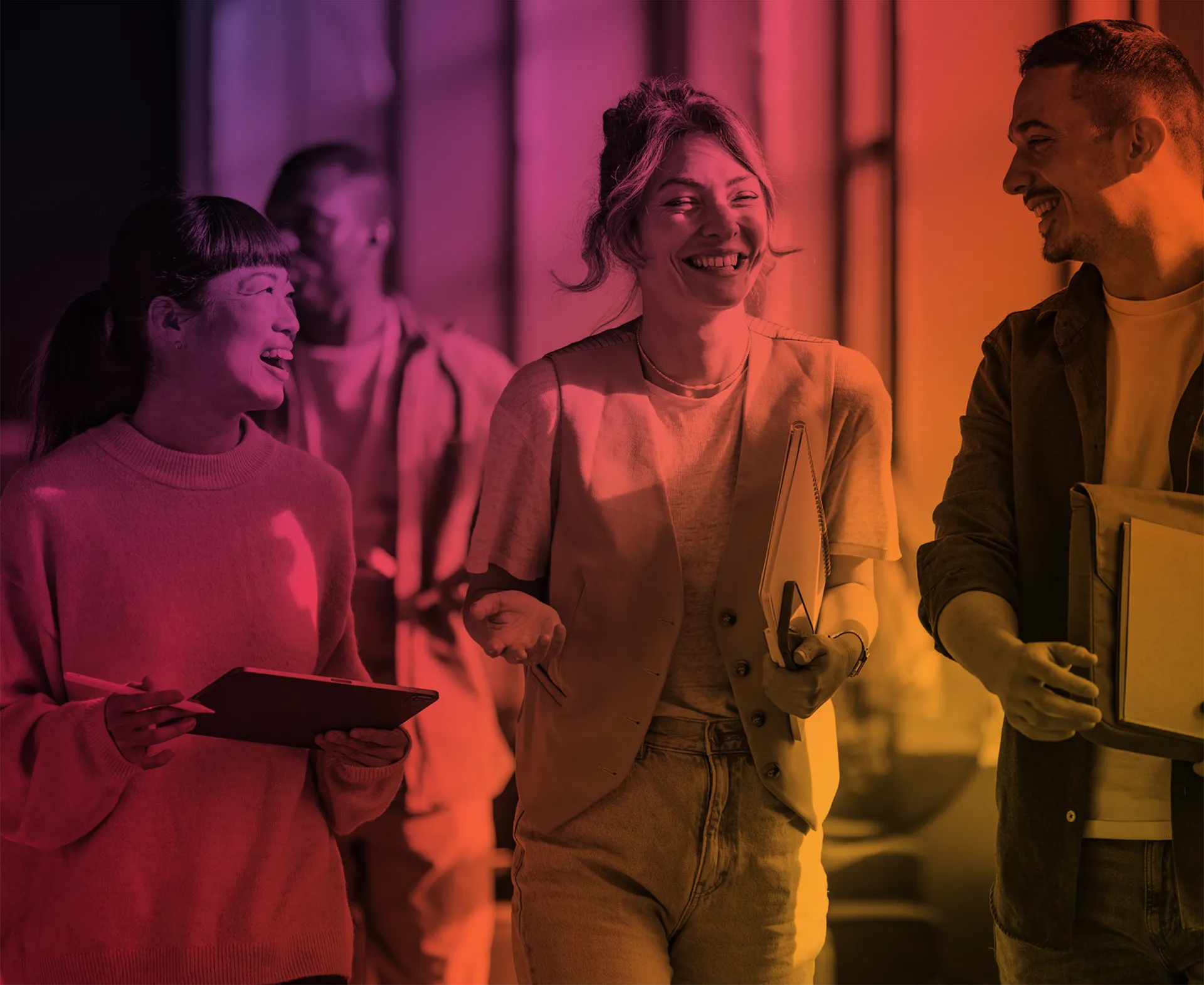 Four colleagues smiling and walking together while holding work materials in a brightly lit office.