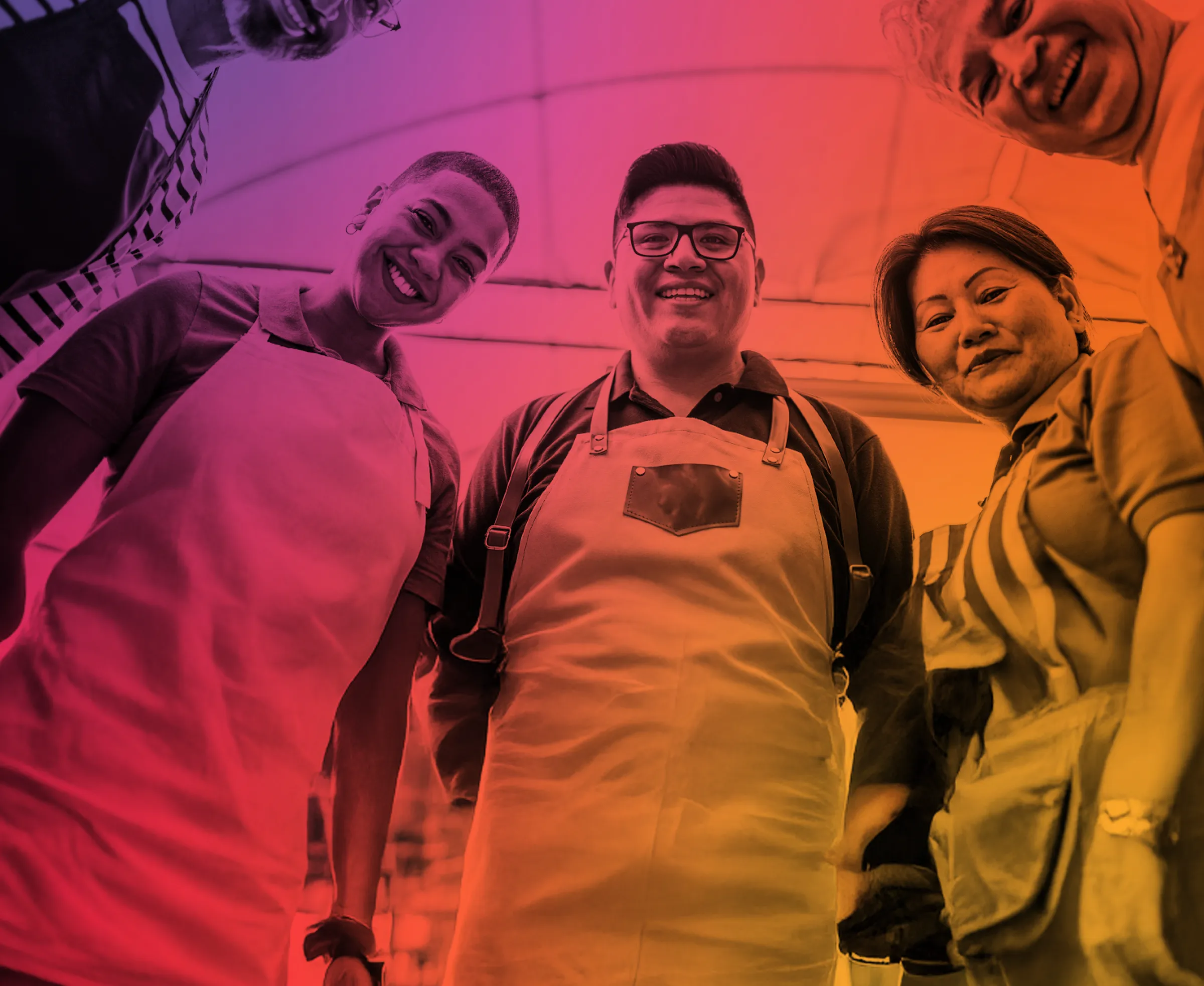 Smiling diverse group of five people wearing aprons standing in a circle, viewed from below with a colorful gradient overlay.