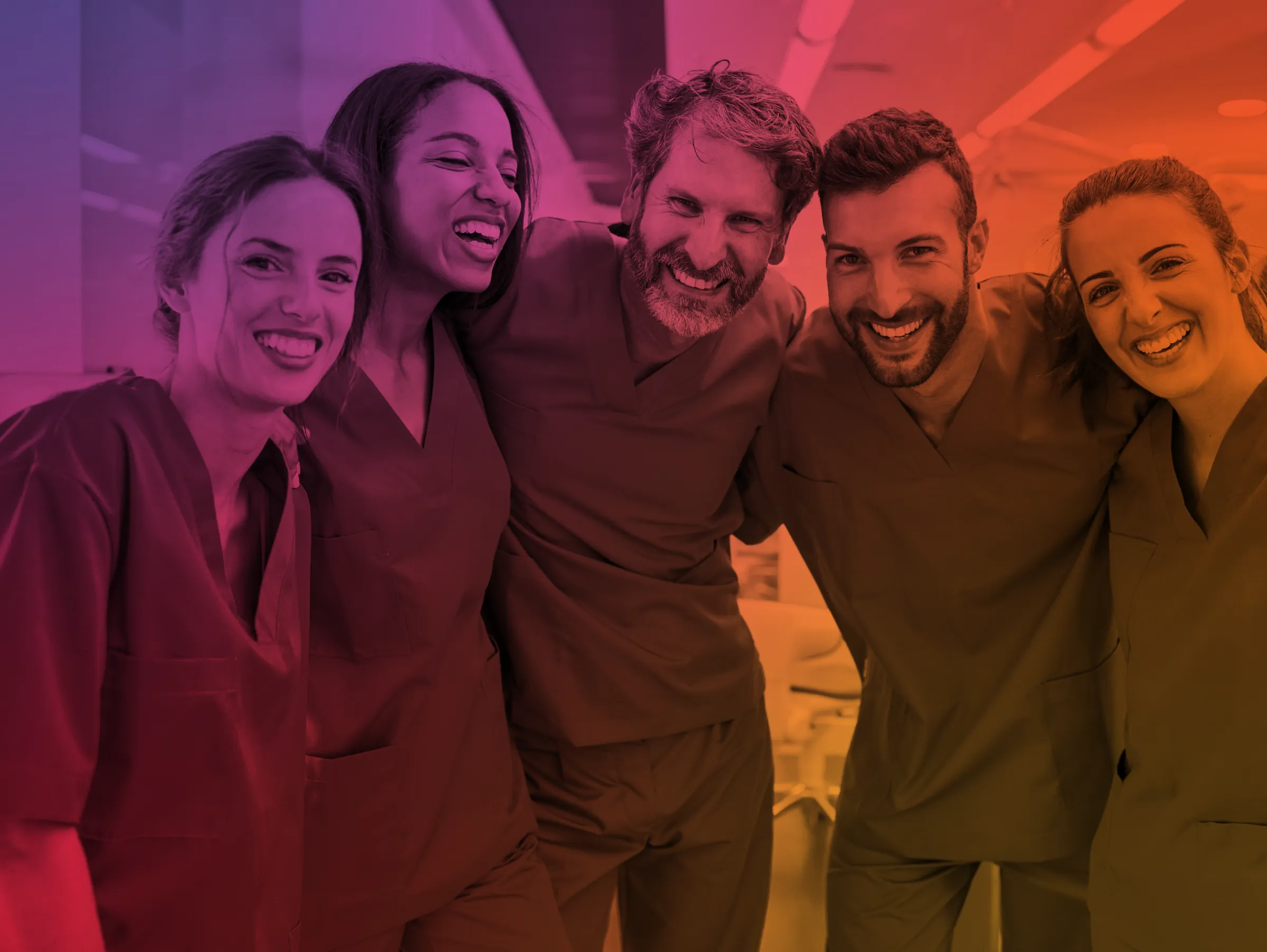 Five healthcare professionals smiling and standing closely together in scrubs in a medical setting.