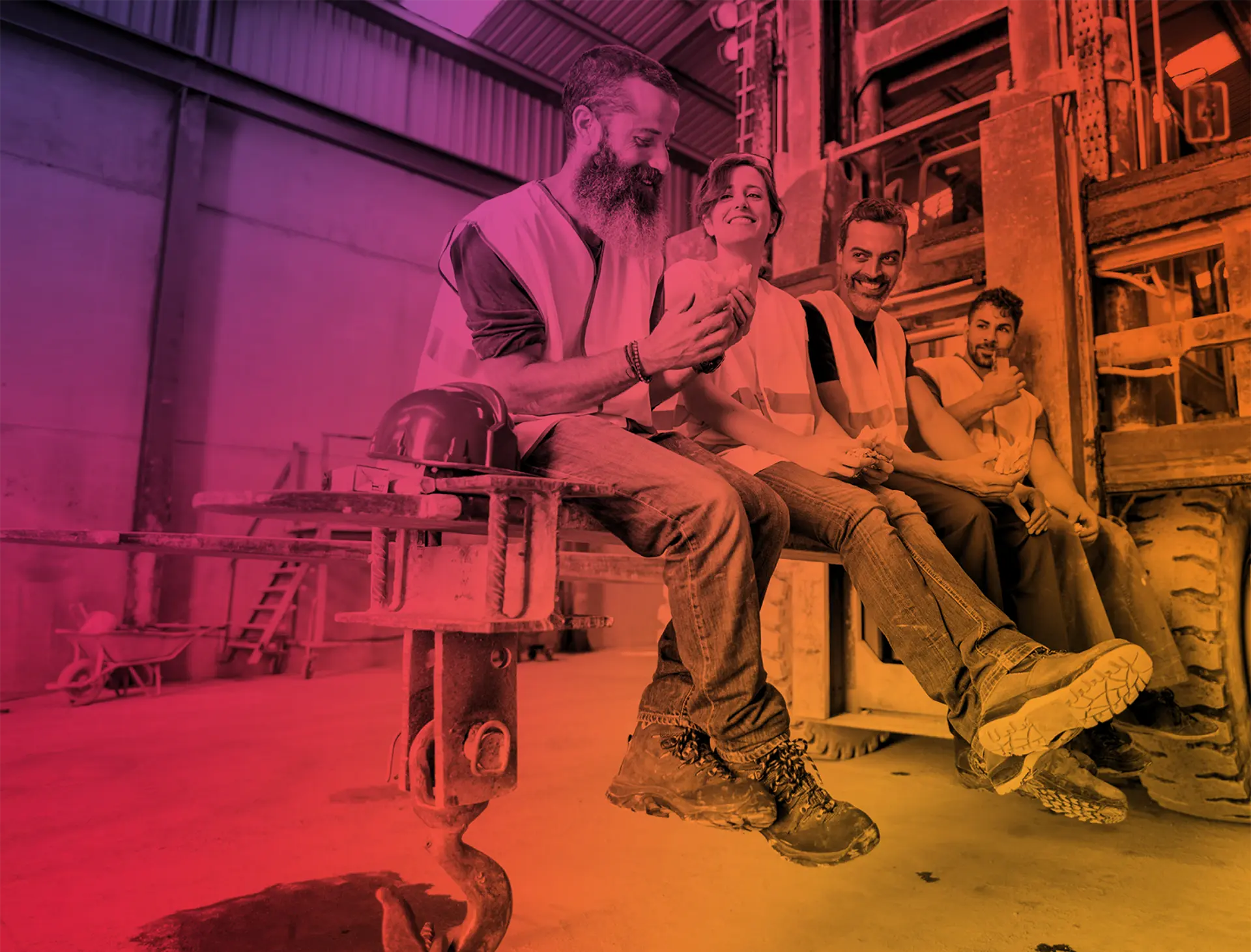 Four construction workers wearing safety vests sitting on industrial equipment enjoying a break together.
