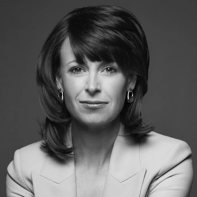Black-and-white headshot of a woman with shoulder-length hair wearing a blazer and earrings, looking directly at the camera with a slight smile.