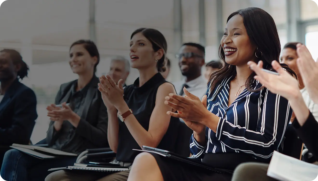 Diverse group of professionals sitting and smiling while clapping in a modern conference room.