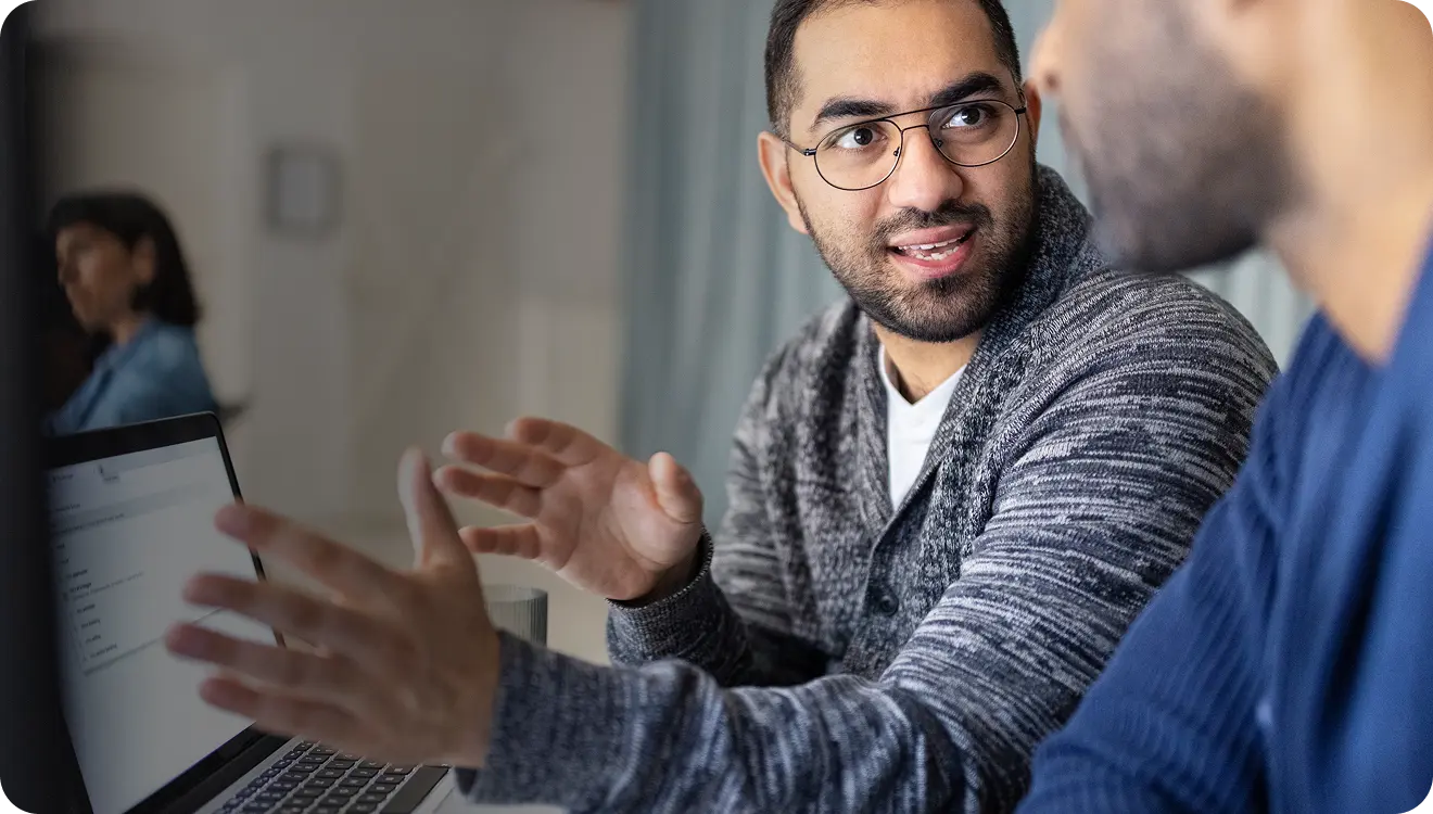 Two men engaged in a discussion while looking at a laptop screen in an office setting.