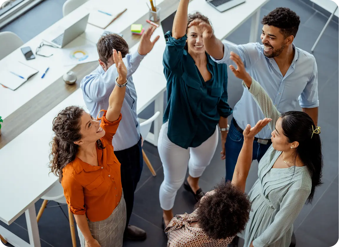 A diverse group of six coworkers smiling and giving high fives in a modern office setting.