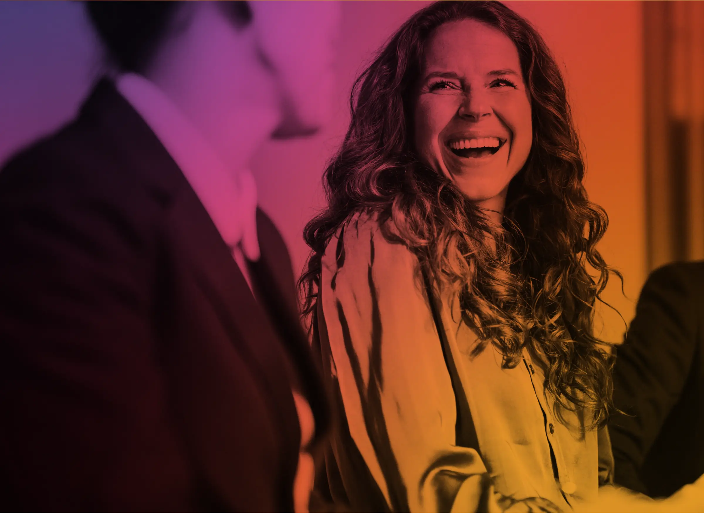 Smiling woman with long curly hair engaging in conversation with a man in a suit.