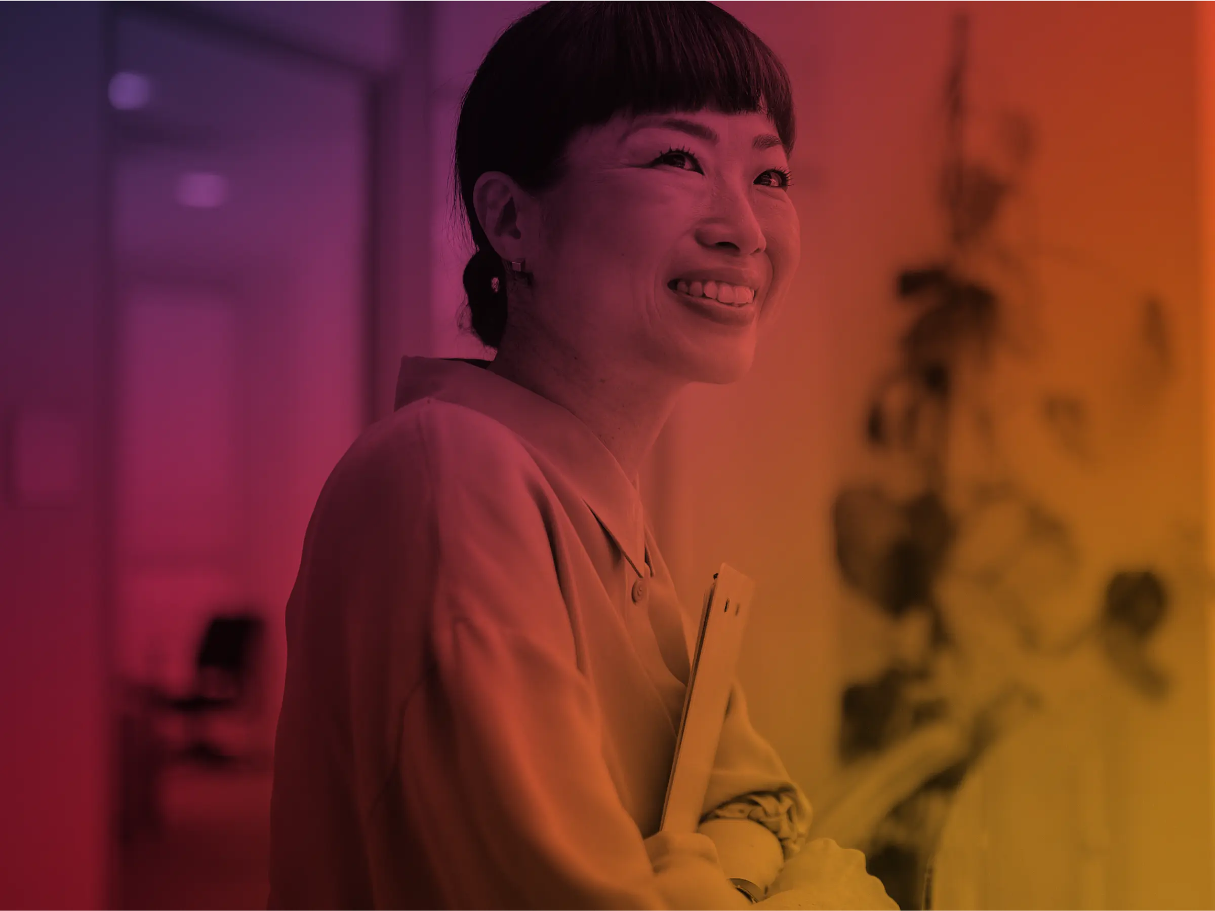Smiling woman holding a clipboard in a softly lit, warmly colored office hallway.