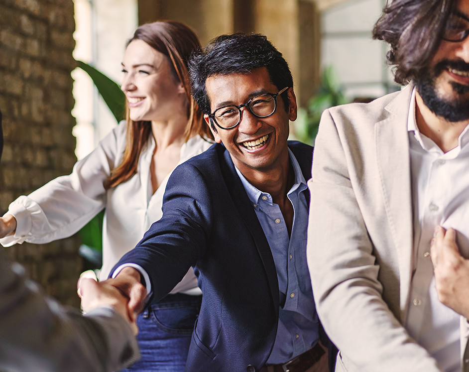 A group of professionals shaking each others hands. The focus is on three men and one woman, and appear to be shaking the hands of people off camera.