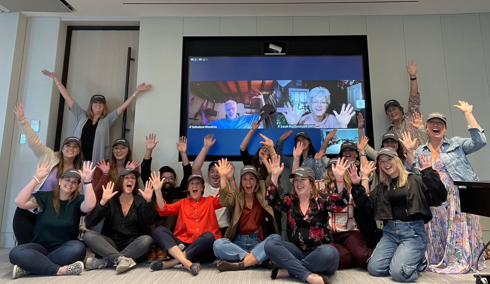 A group of company employees wearing matching hats, smiling with their hands raised in a celebratory way.