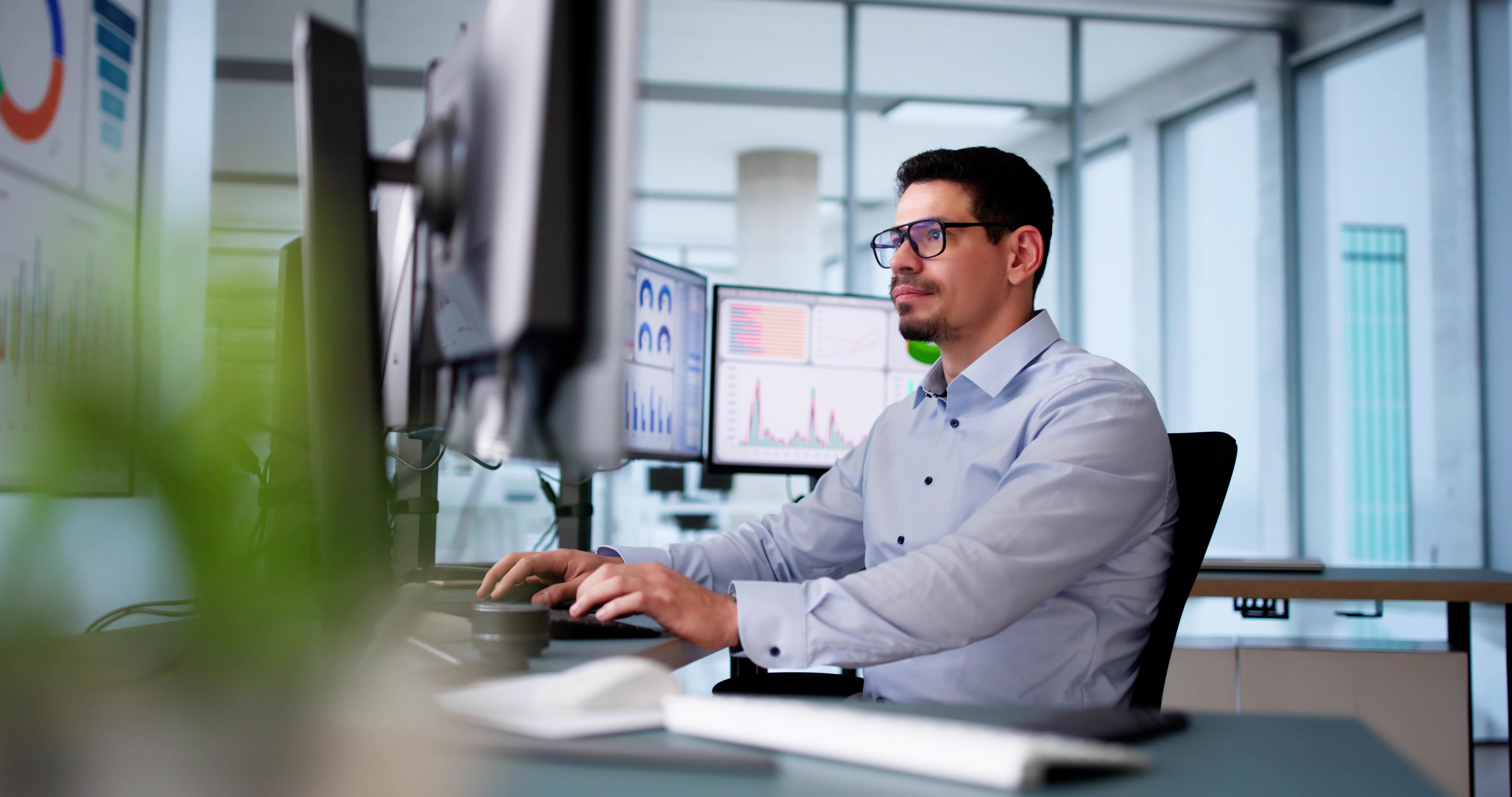 A professional looking man sitting at a desk typing with four computer monitors around him.