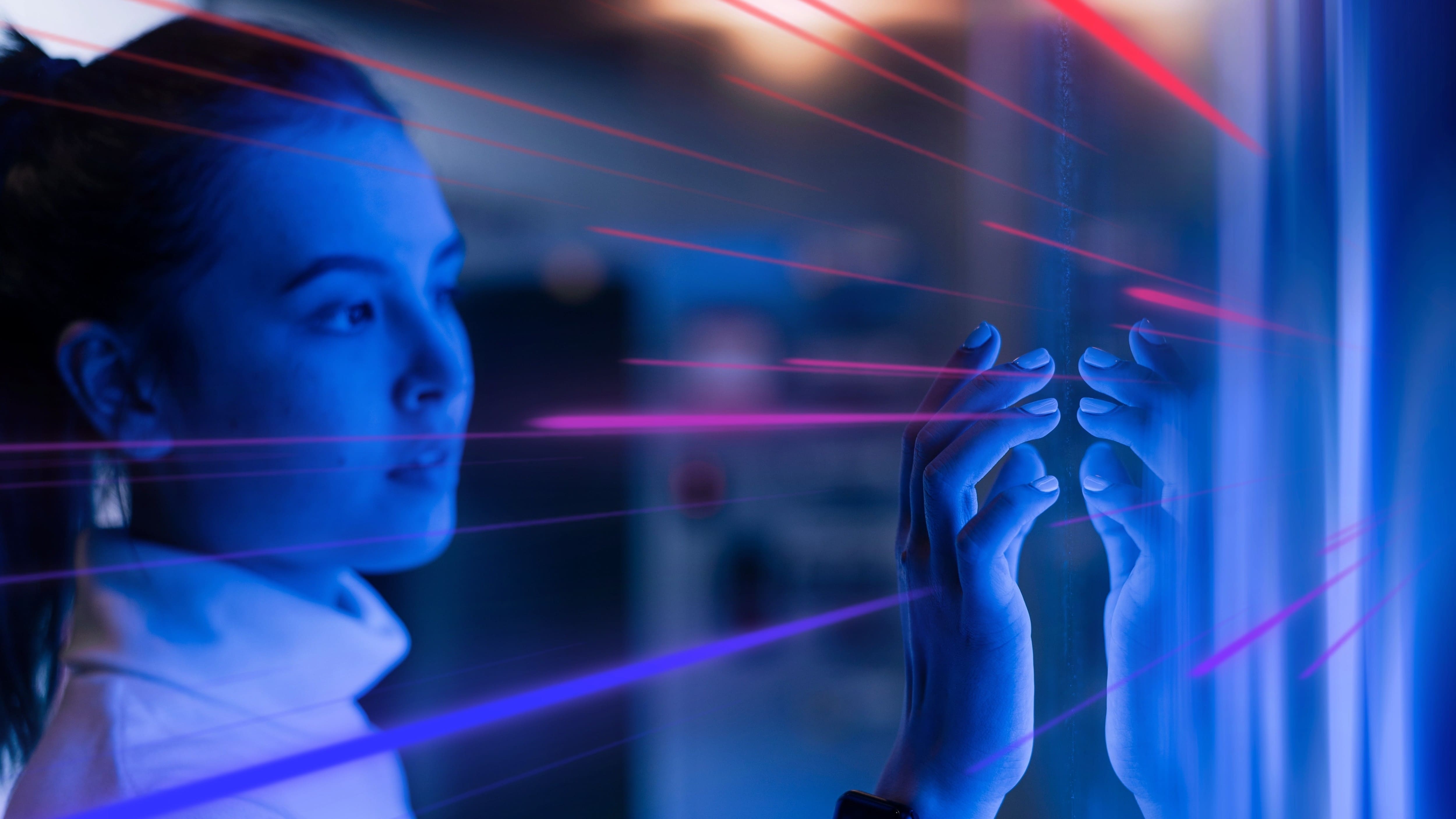 A woman interacts with a futuristic digital interface, in a dark space with blue lights.