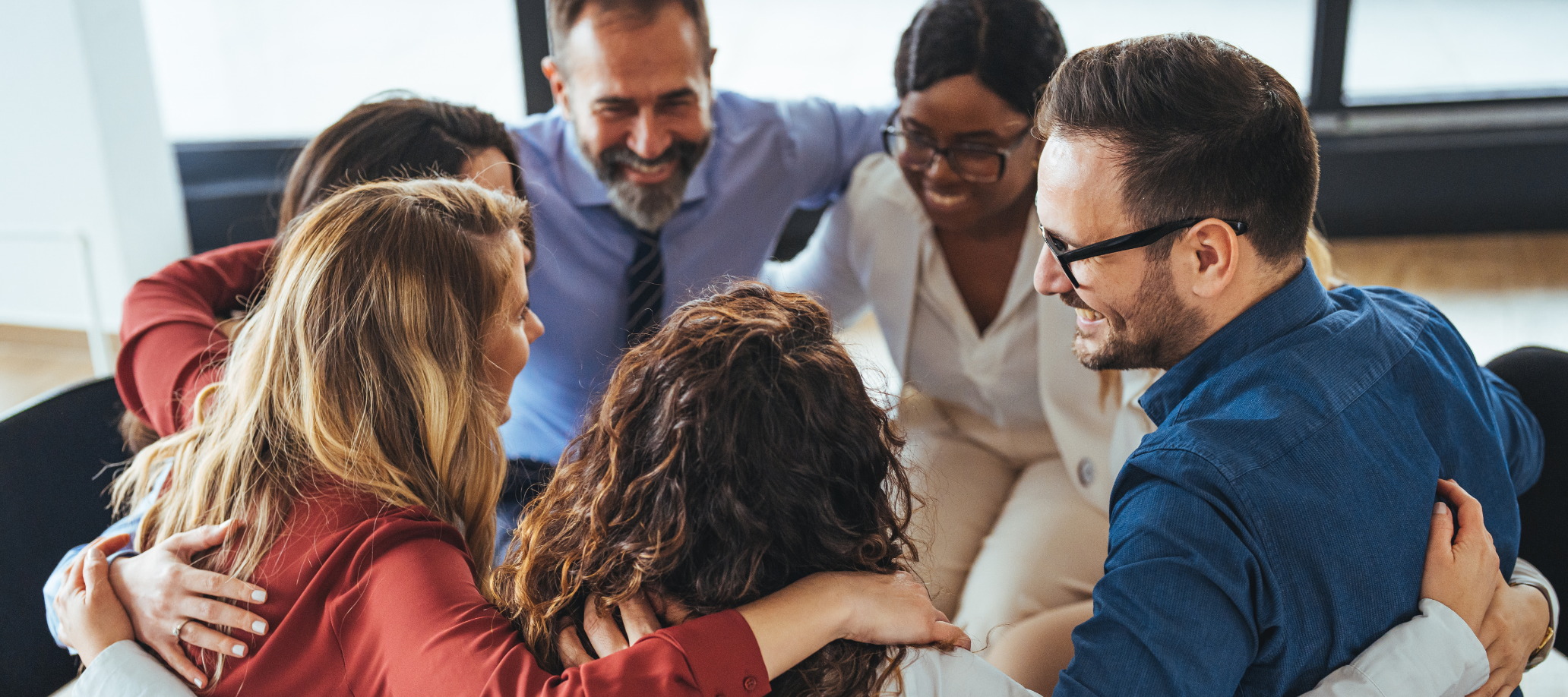 A group of professionals with their arms around each other in a circle, smiling at each other.