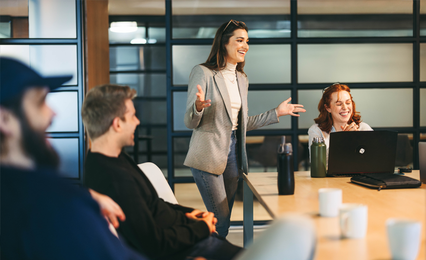 Grou of professionals sitting around a table, with one woman standing up and presenting to them.