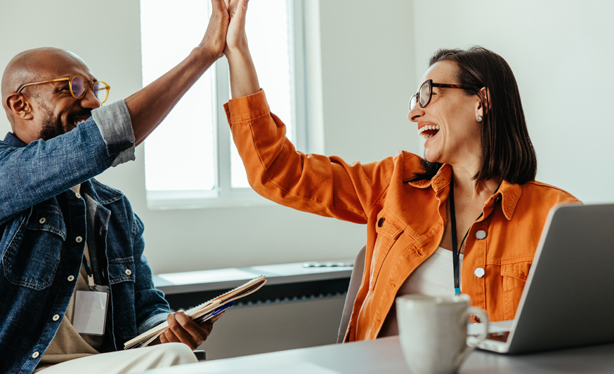 A man and woman sitting at a desk and high fiving each other.