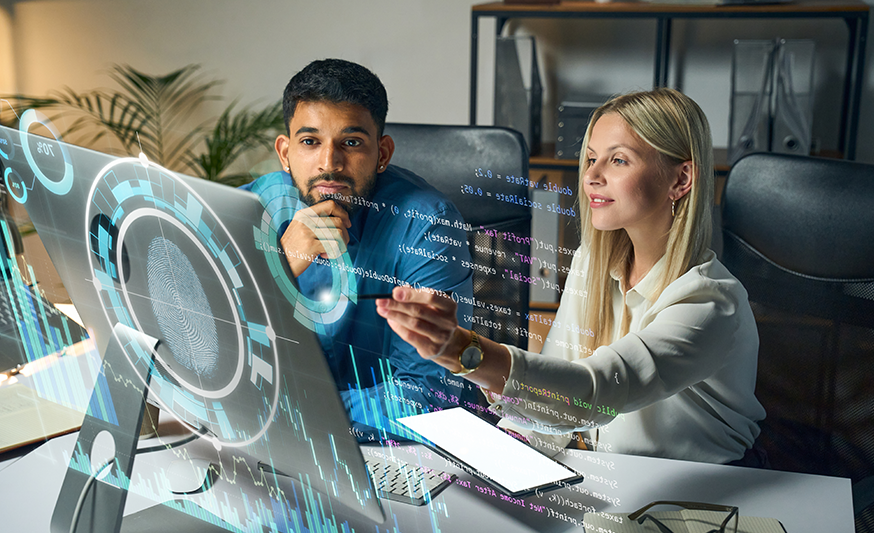 A man and woman professional are sitting at a desk in front of a computer monitor, and the text from the computer screen is overlayed so we can see what they're looking at.