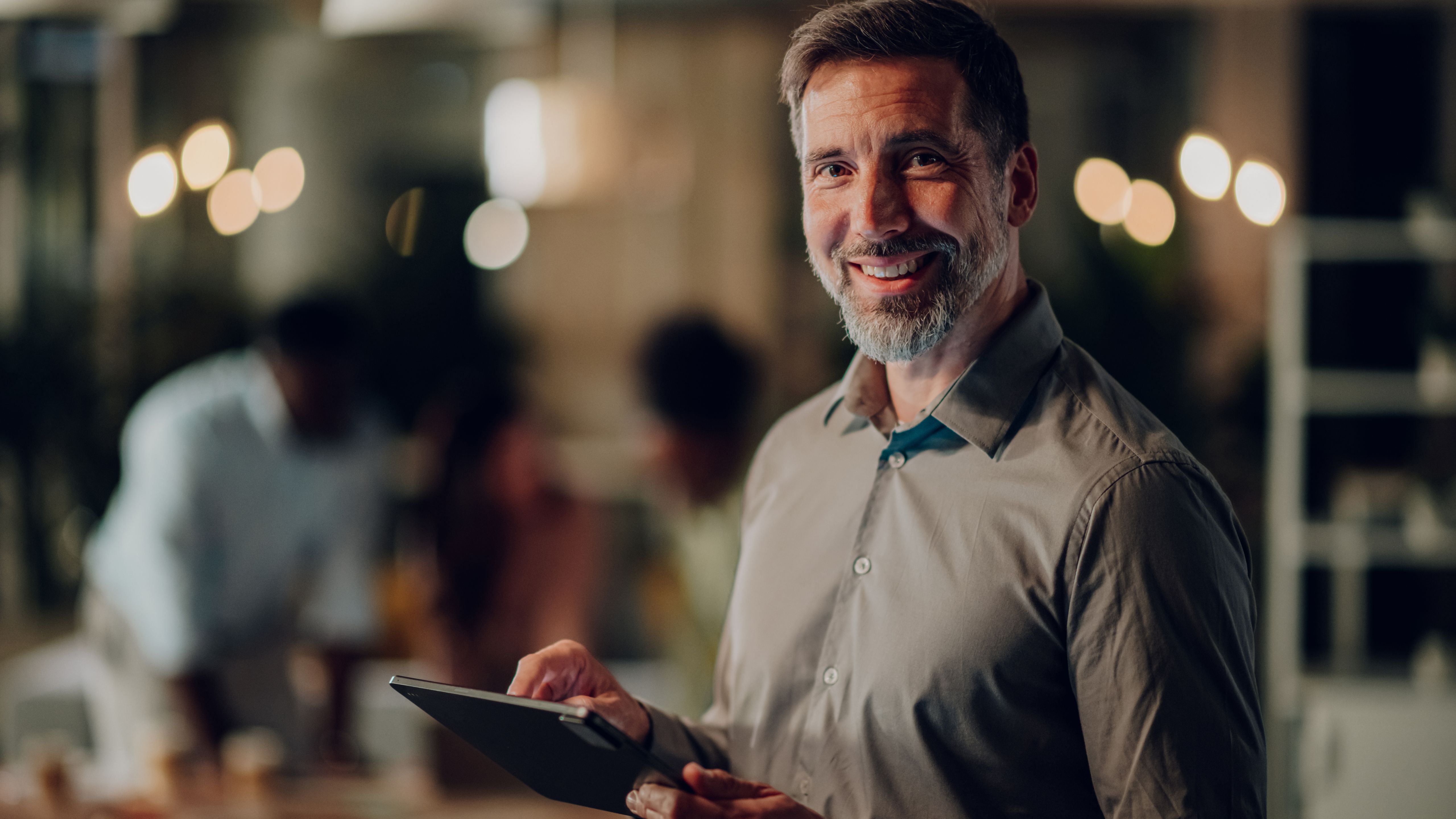 Image of a man smiling at the camera in a button down shirt, holding a tablet.