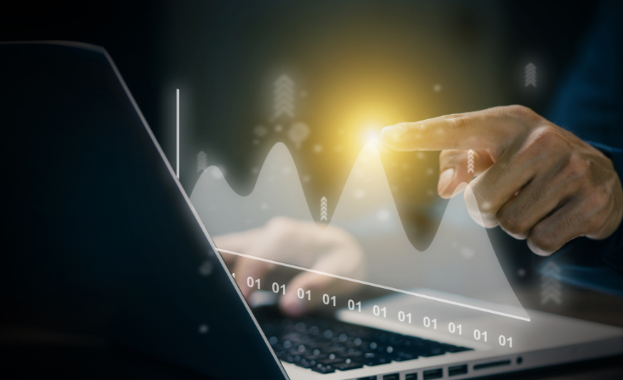 A laptop open, facing away from camera, with a 3D graph showing and a hand pointing to a point on the graph. 