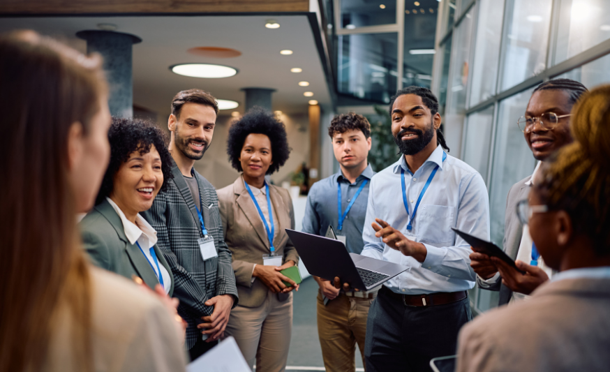 A group of tech professionals standing in a circle talking, with one man holding a computer in his hand and he appears to be talking.