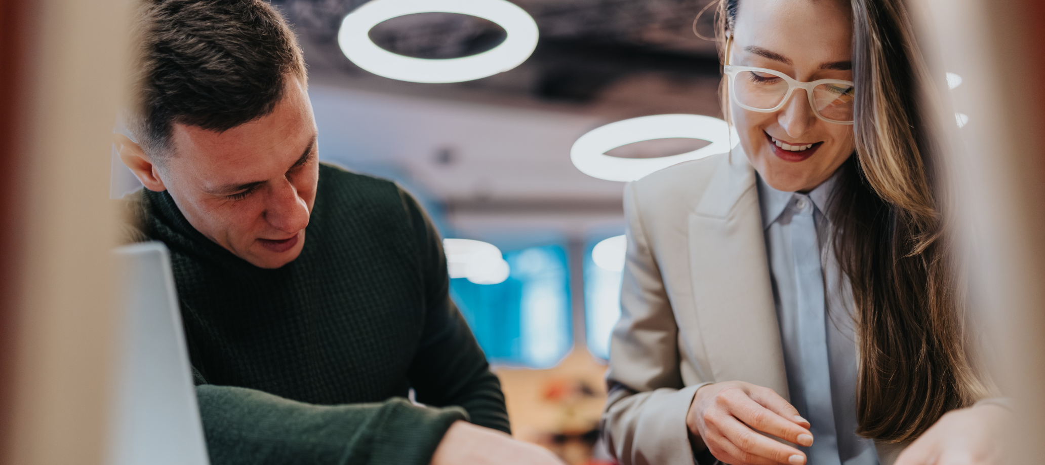 Two professionals working together at a desk, with a bright light behind them.