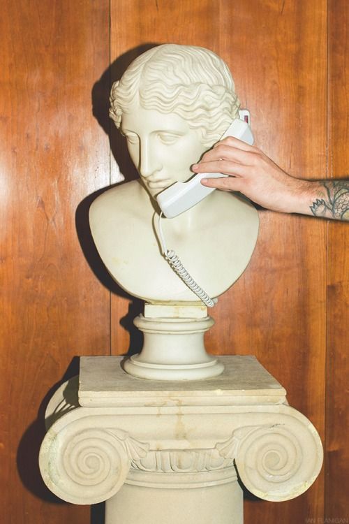 Un buste classique en marbre tenant un téléphone fixe blanc contre son oreille par une main tatouée.