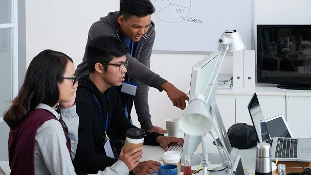 Three young professionals collaborating and looking at a computer screen in an office setting.