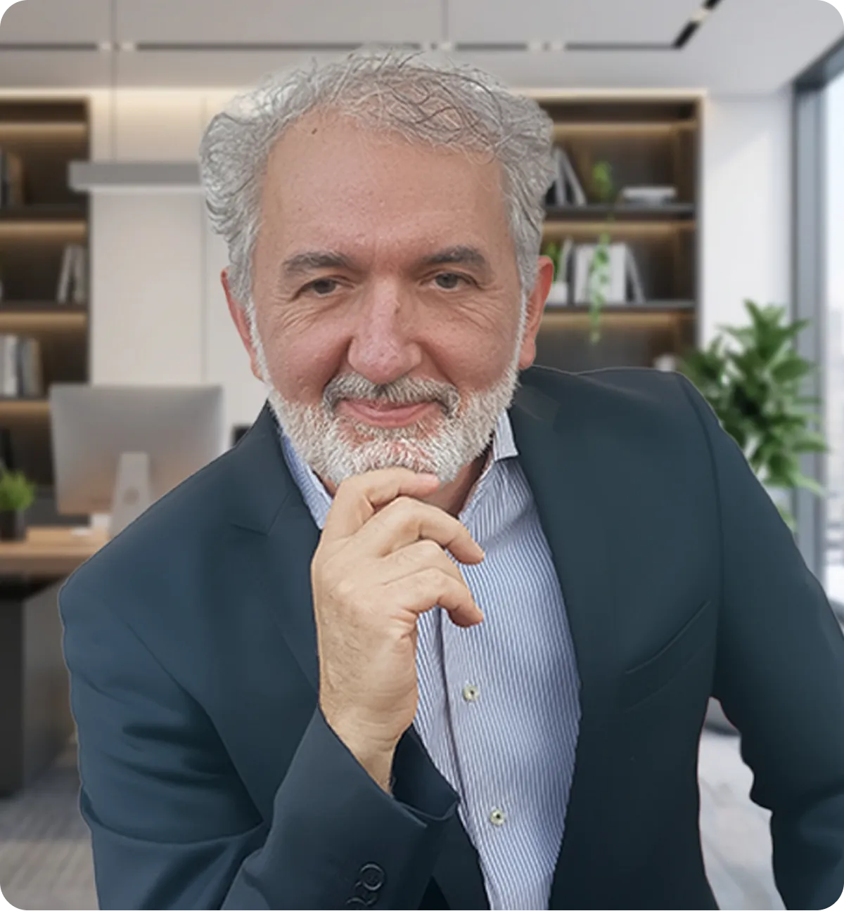 Smiling middle-aged man with gray hair and beard wearing a navy blazer and striped shirt, posing thoughtfully in a modern office.