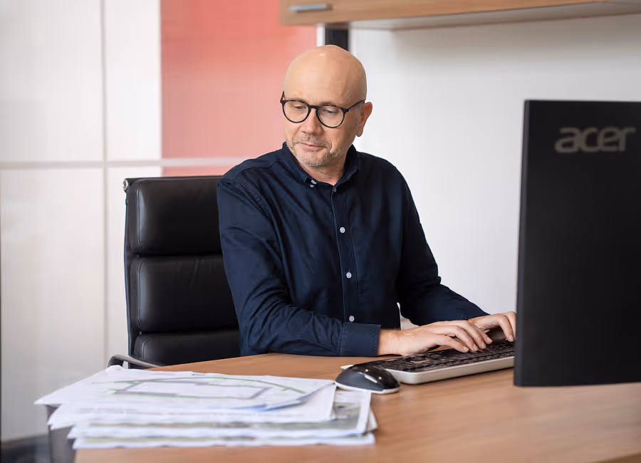man with glasses working on computer inspecting plans