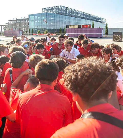 Large group of children and a few adults in red shirts gathered outdoors near a modern glass building with a diner sign.