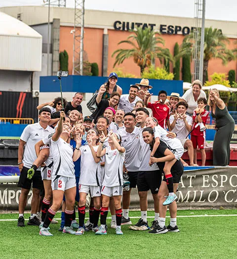 Youth soccer team and coaches smiling and posing for a group selfie on a soccer field.