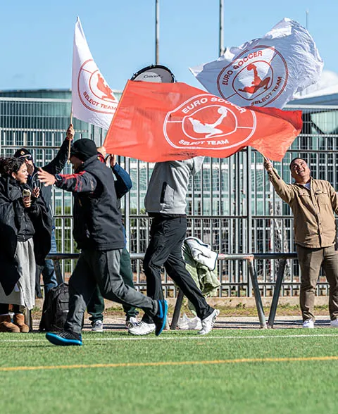 People on a soccer field waving white and orange flags with a Euro Soccer Select Team logo.
