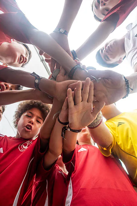 Young soccer players in red and yellow jerseys putting their hands together in a team huddle.