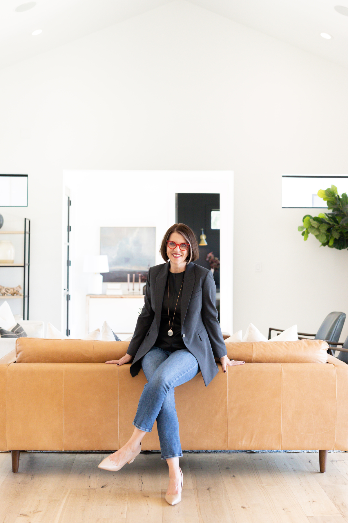 Woman with red glasses sits on tan leather couch in a bright, modern living room.