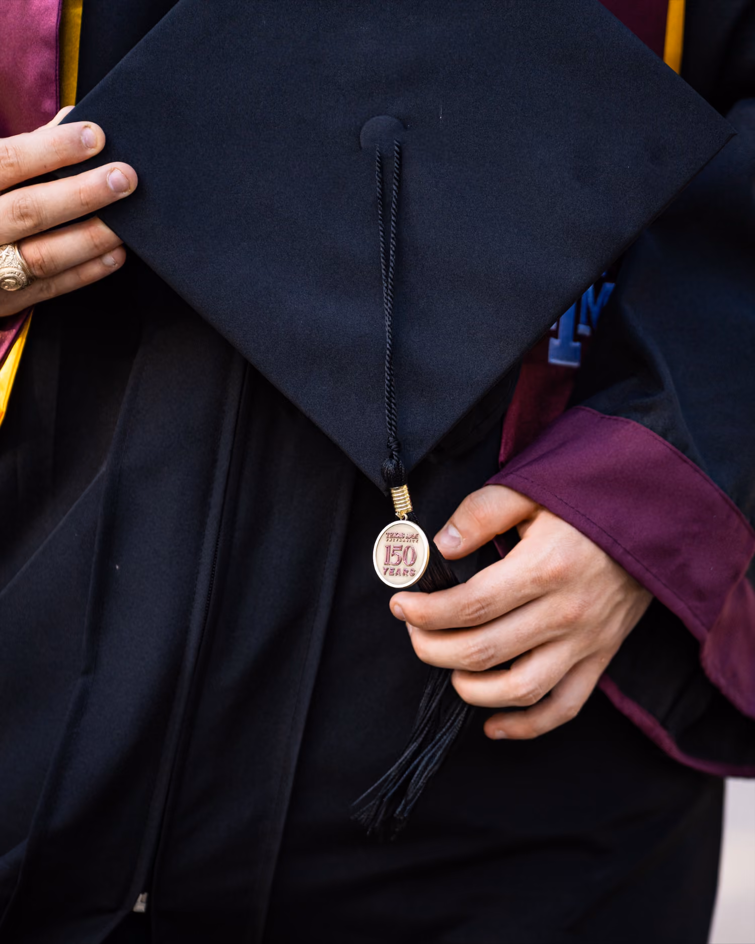 A graduate holding a black cap with a tassel and a medallion reading 'Texas A&M University 150 years'.