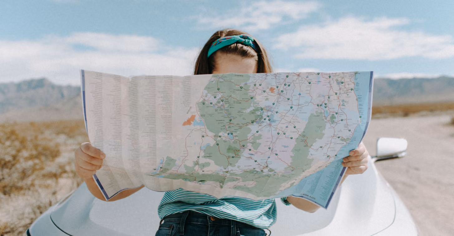 Person sitting on a white car outdoors holding and looking at a large unfolded map.