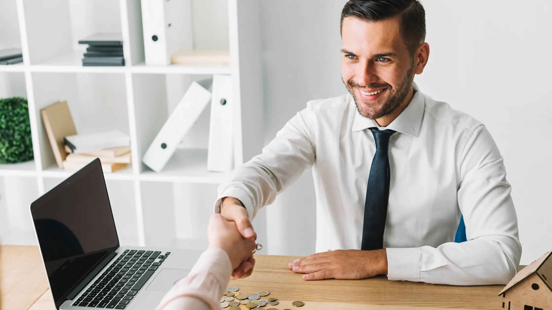 A man in a business setting shaking hands with another person, with coins on the desk, potentially representing a discussion about business loan options for an electrician.