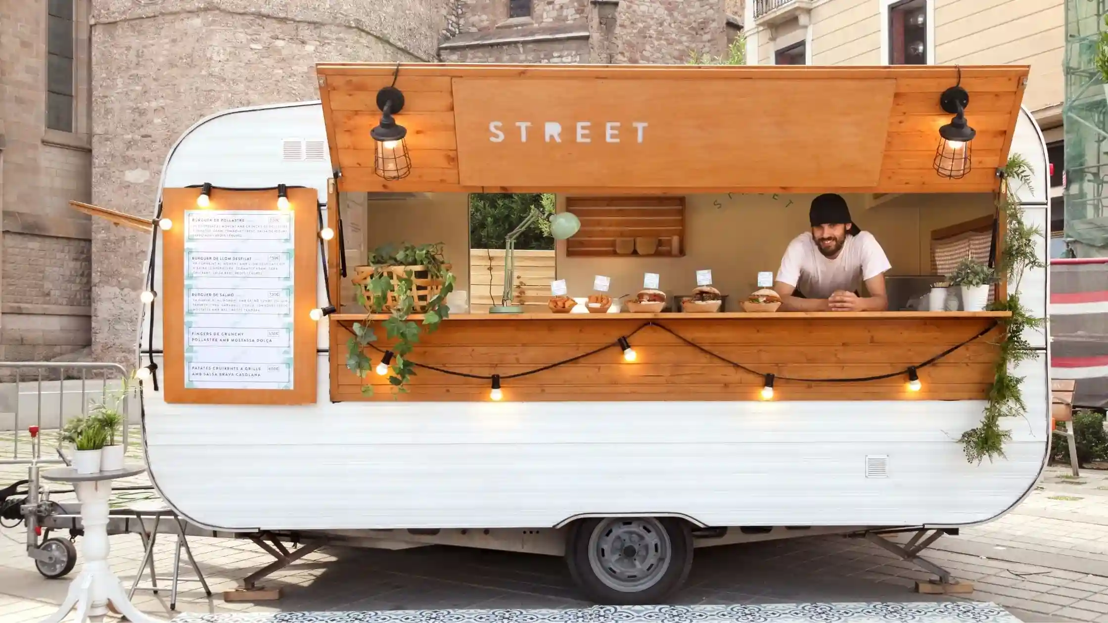  A vendor smiling from inside a food truck with string lights.