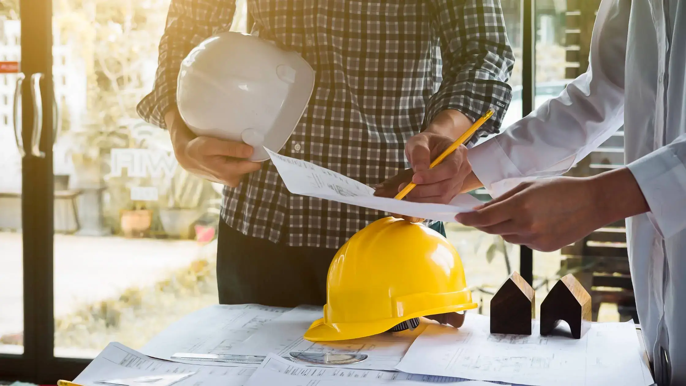  Two people at a desk with blueprints and hard hats, discussing a construction company loan project.