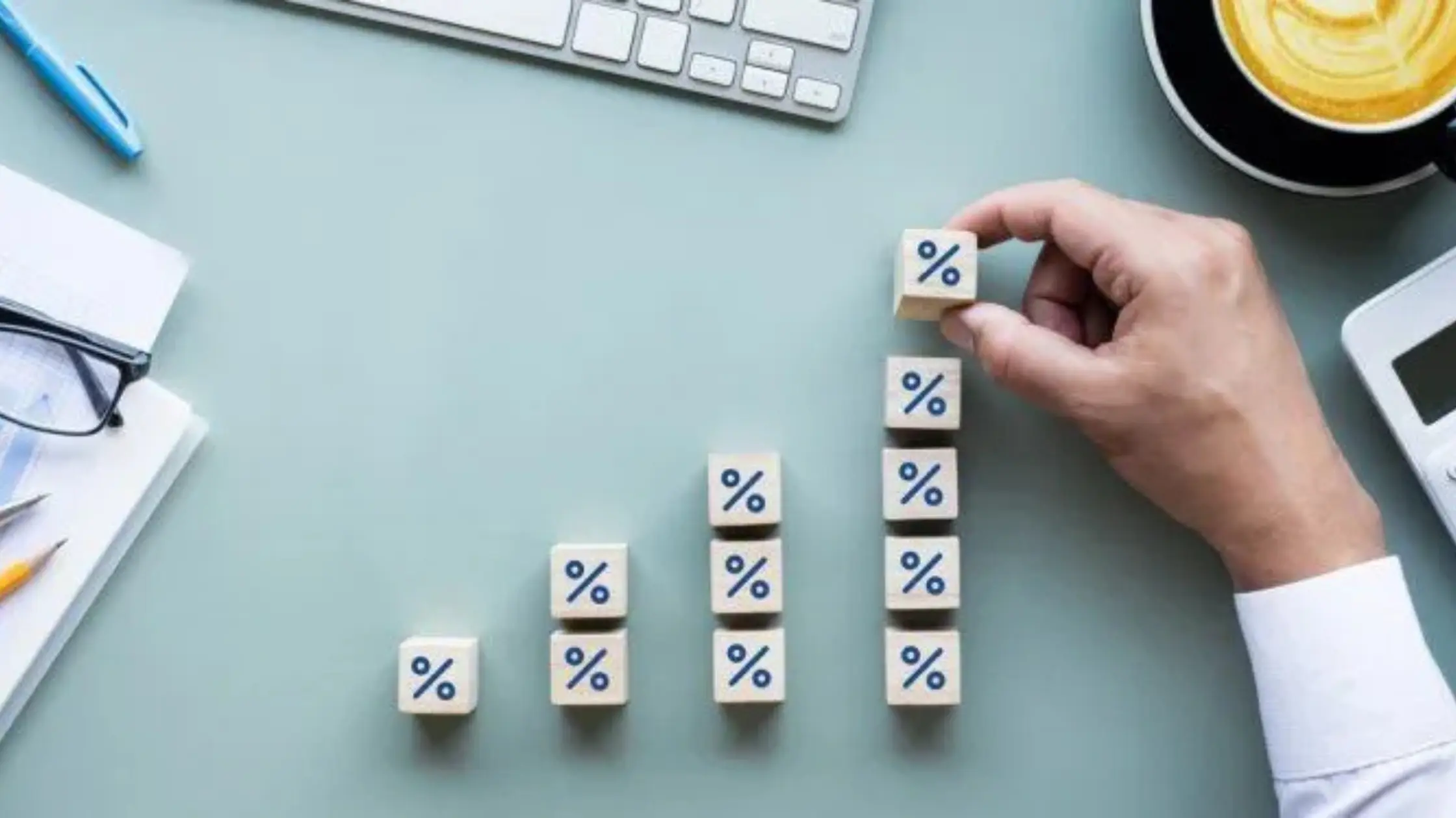  A hand places a wooden block with a percentage symbol on top of a growing stack of similar blocks, representing a factor rate. 