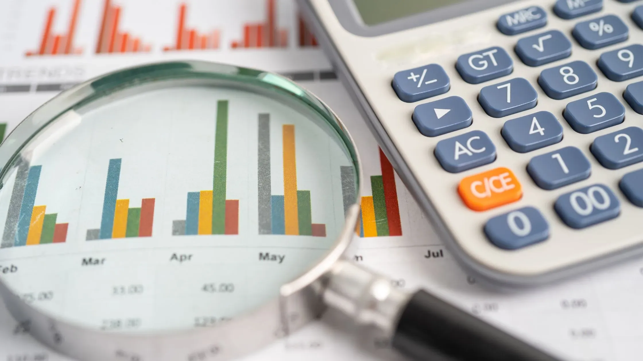  A magnifying glass is positioned over a paper with a bar graph and a calculator is next to it representing annual percentage rate.