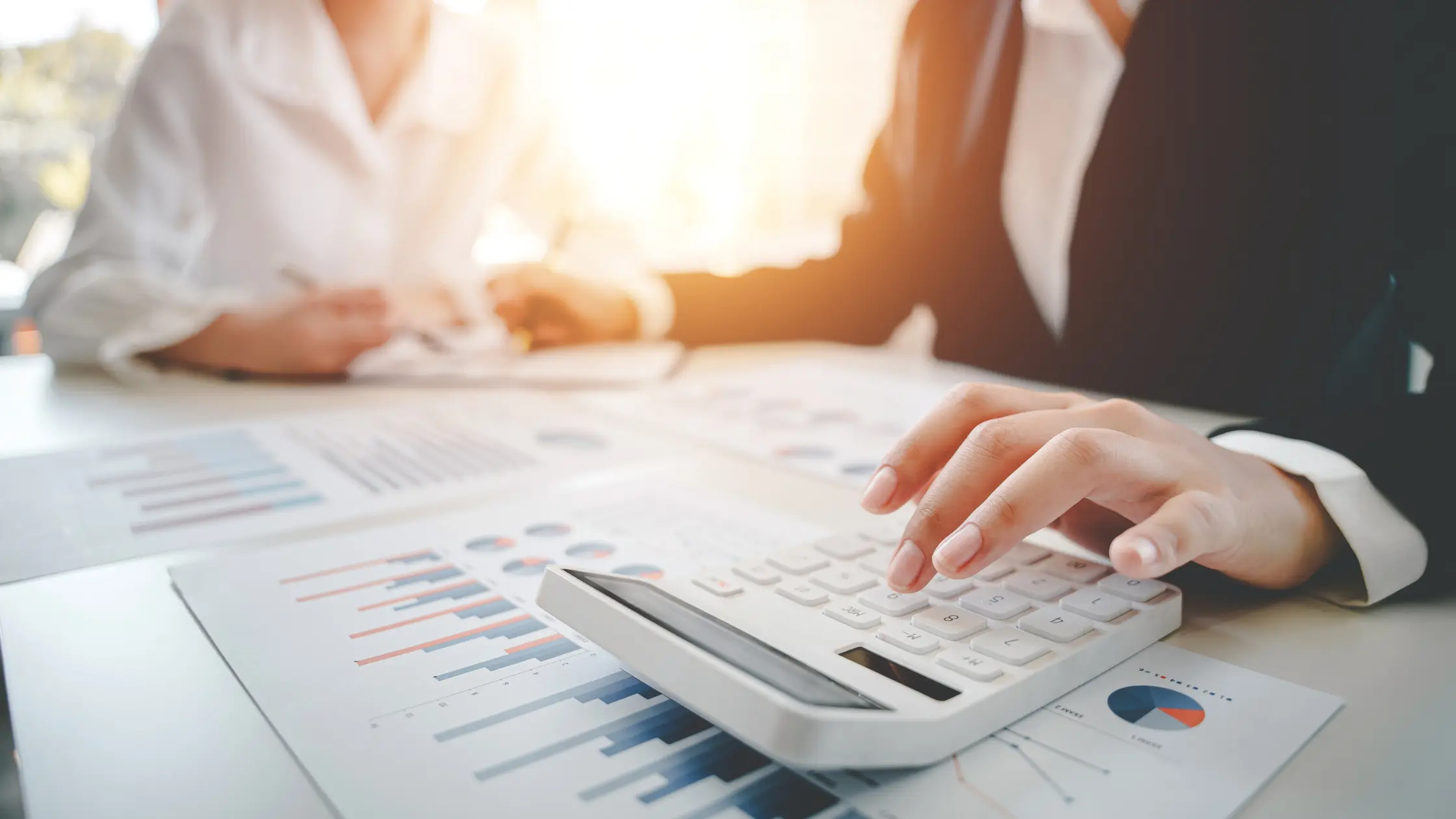 Hand calculating finances with charts, discussing Business Credit strategy.
