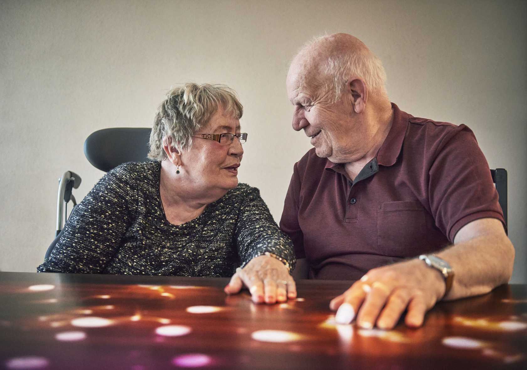 Un homme et une femme âgés assis côte à côte à une table, se regardant en souriant, lors d'une séance avec la Tovertafel dont les projections lumineuses sont visibles sur la surface de la table.