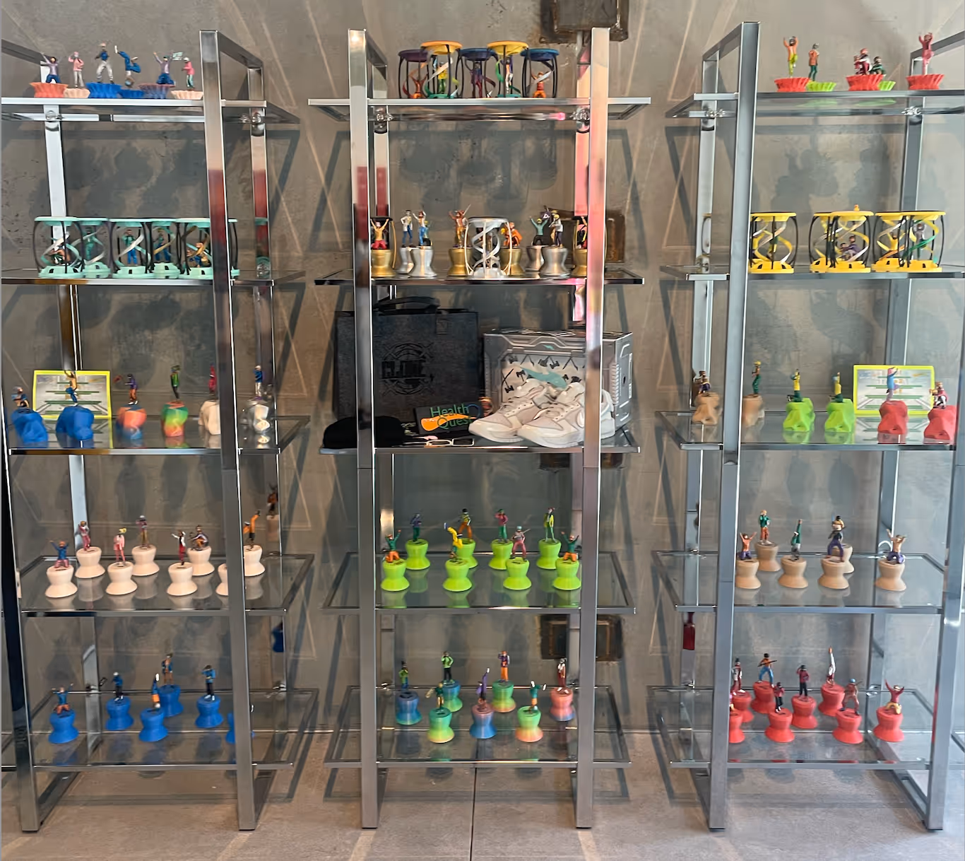 All 99 physical Health Quest totems are displayed on three shelving units. The middle shelf includes a "Health Quest" sign and two pairs of athletic shoes.