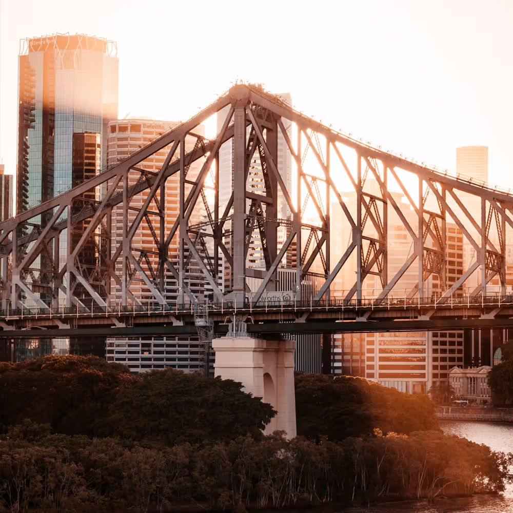 The Storey Bridge with Brisbane city skyscrapers in the background at sunset.