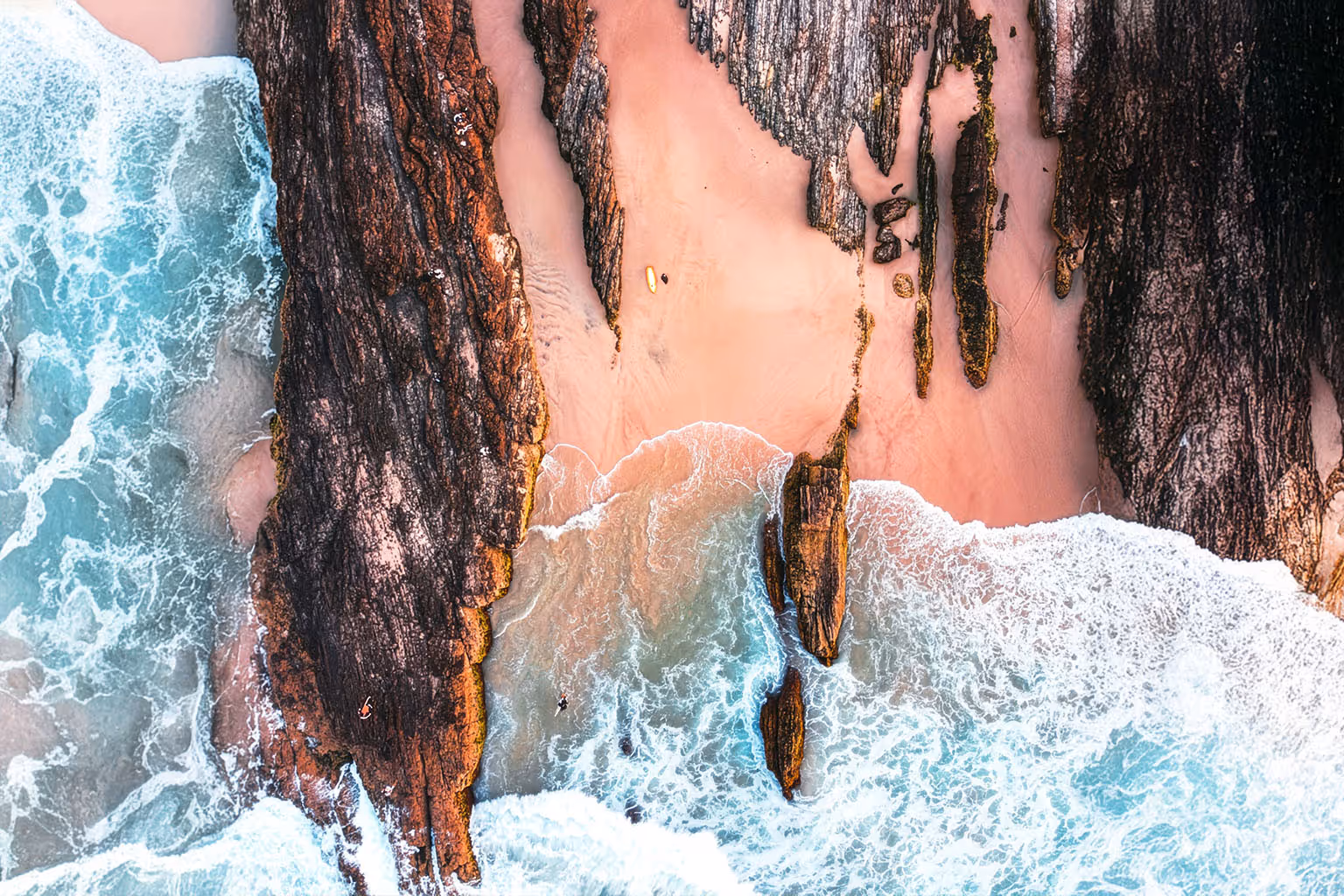 Aerial view of rocky coastline with waves crashing onto sandy beach and people in the water.