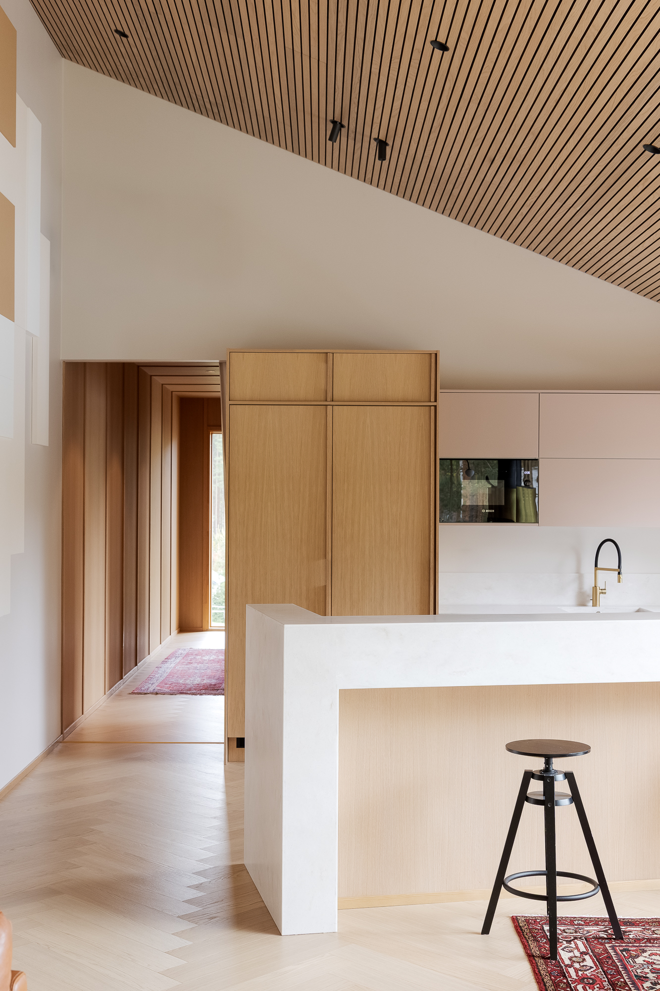 Modern kitchen with wooden cabinets, a white marble island, black stool, and a patterned rug on light wood flooring.