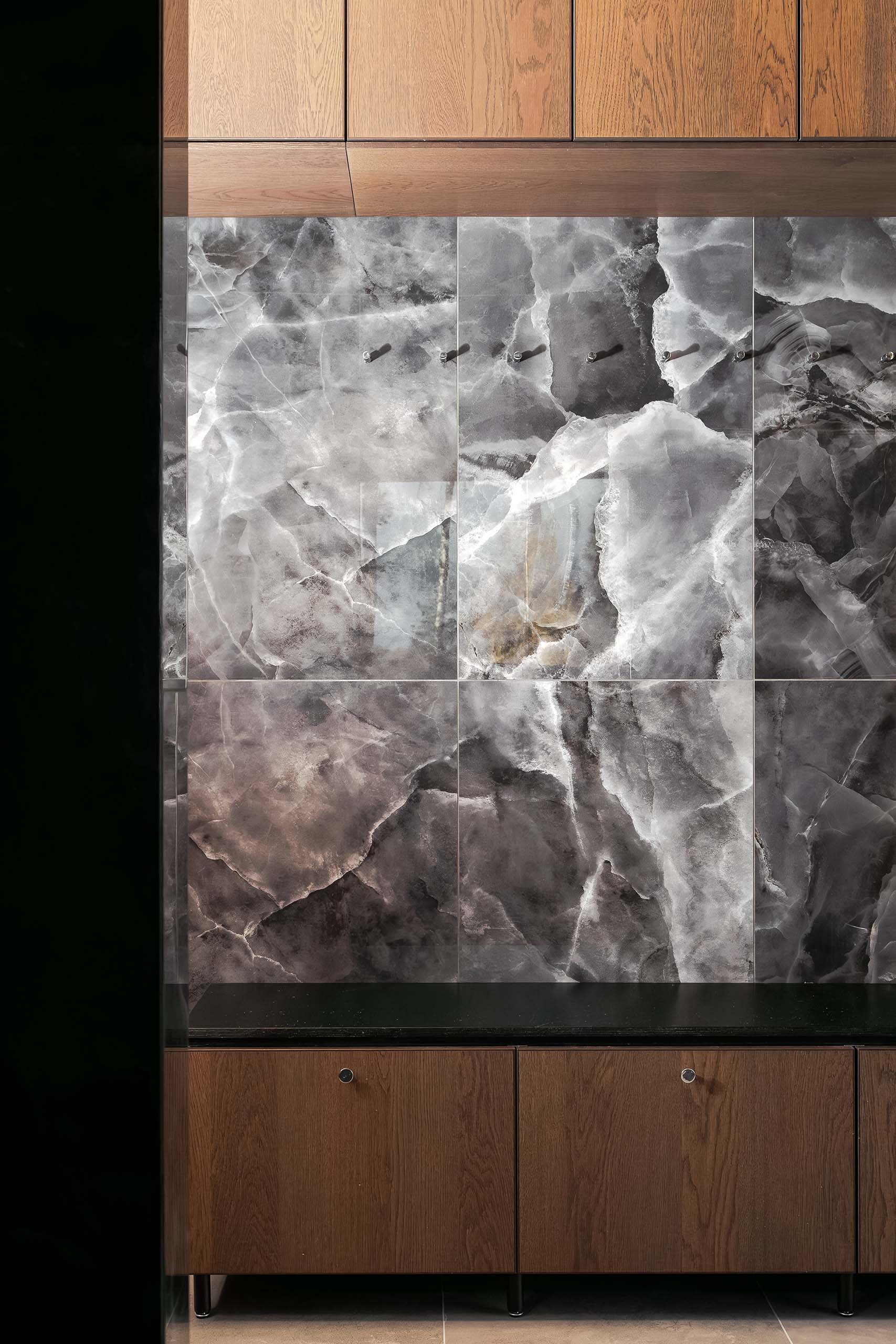 Kitchen backsplash with large gray marble tiles between wooden upper and lower cabinets with a black countertop.