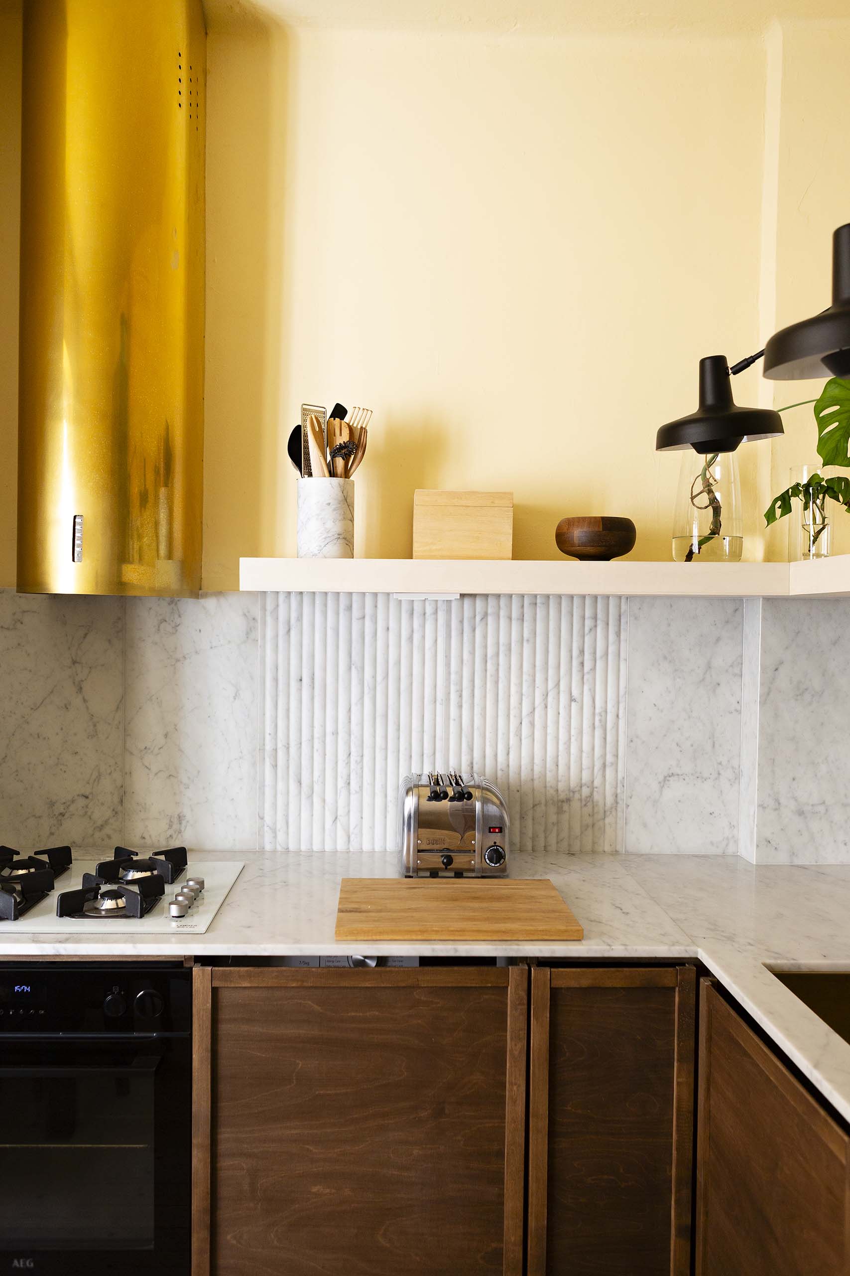 Modern kitchen countertop with marble backsplash, gas stove, wooden cabinets, cutting board, toaster, and a utensil holder.