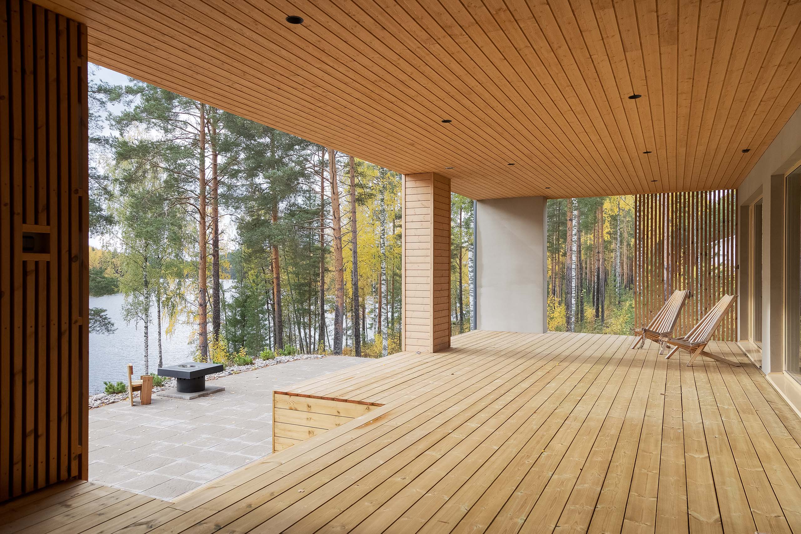 Spacious wooden deck with two striped lounge chairs overlooking a forest and lake.