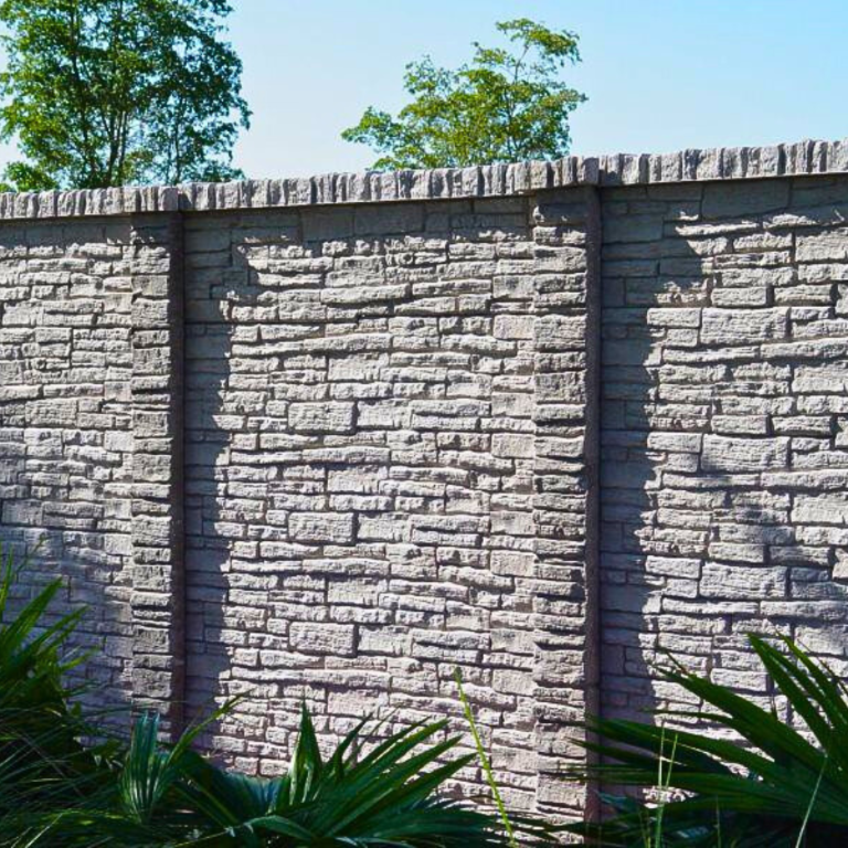 A close-up of a light grey precast concrete fence panel featuring a textured, irregular stacked stone pattern and a decorative cap border. Dark green foliage is visible along the base.